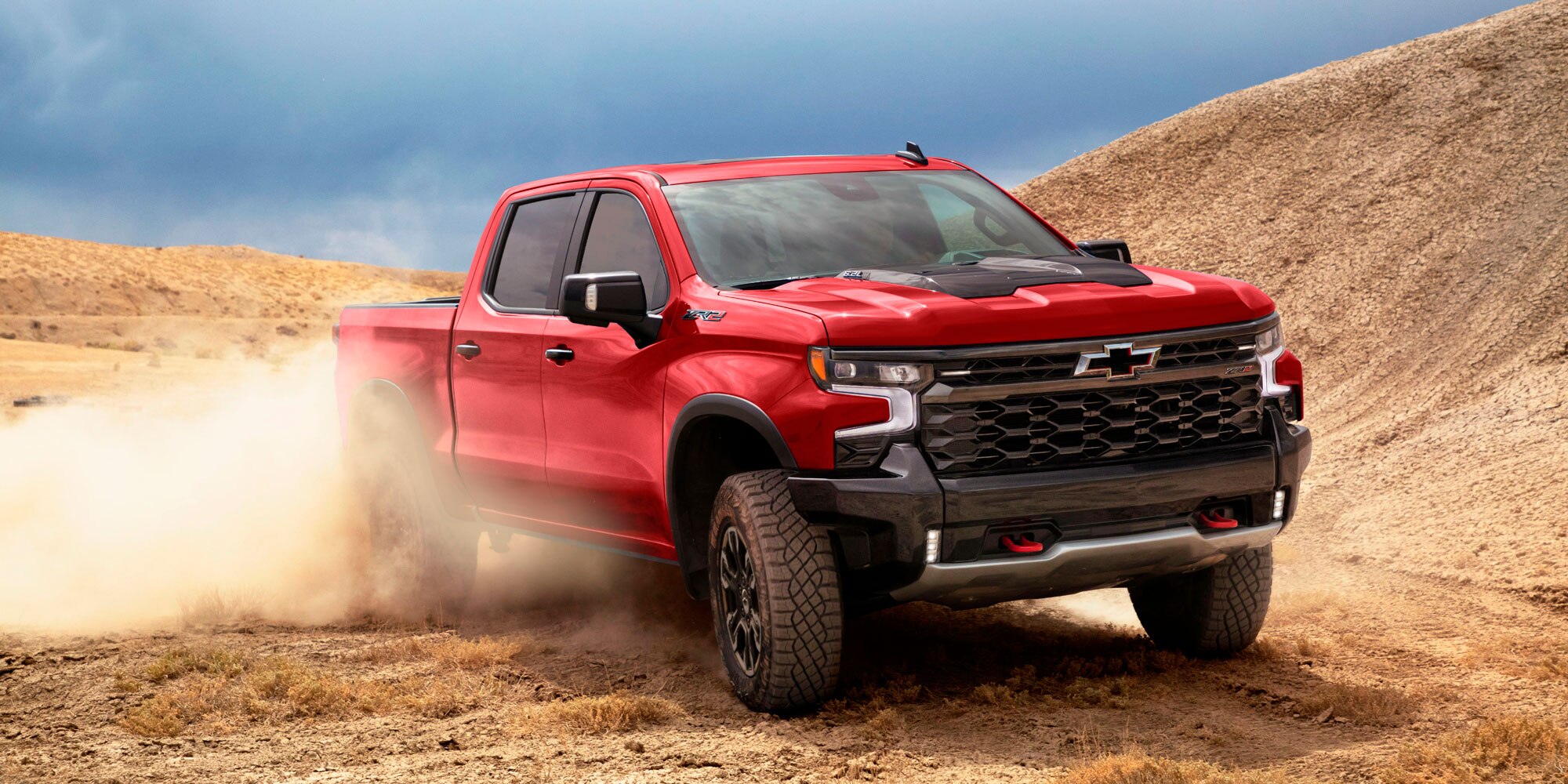 Chevrolet Silverado roja avanzando sobre terreno arenoso con polvo.